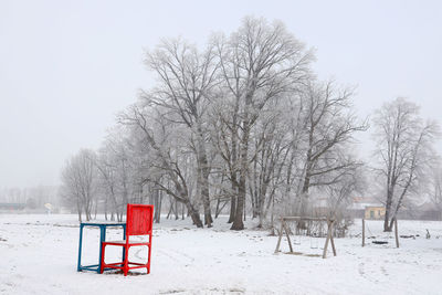 Bare trees on snow covered field against sky