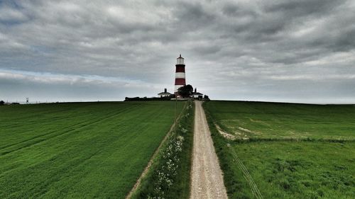 Happisburgh lighthouse on field against cloudy sky