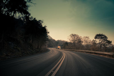 Road by trees against sky during sunset