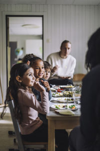 Smiling girl talking with teacher by classmates having breakfast in kindergarten