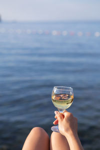 A girl holds in her hand a glass of white wine against the backdrop of a beautiful blue sea.