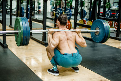 Man in squatting position weightlifting at gym