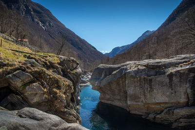 Scenic view of river by mountains against clear blue sky