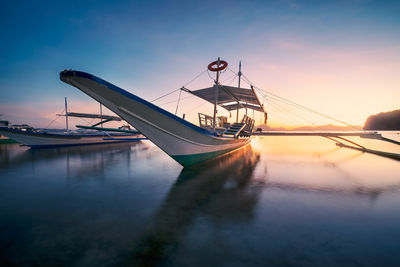 Sailboat moored on sea against sky during sunset