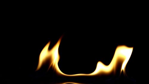 Close-up of burning candle against black background