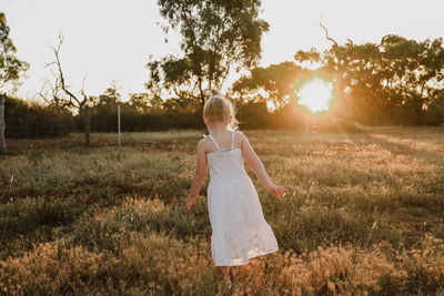 Woman standing on field against sky during sunset