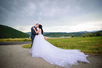 Bridal couple kissing on road against sky