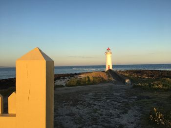 Lighthouse by sea against clear blue sky