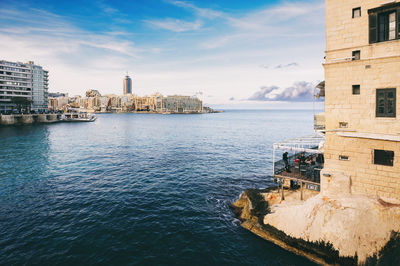 View of city at waterfront against cloudy sky