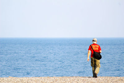 Rear view full length of man walking at beach against clear sky