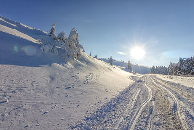 Tire tracks on snow covered land against bright sun