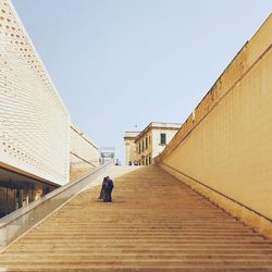 Woman walking on walkway amidst buildings against sky