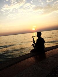 Silhouette man sitting on beach against sky during sunset