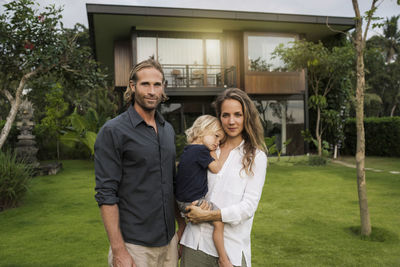 Portrait of smiling family standing in front of their design house surrounded by lush tropical garden