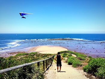 Rear view of man standing on steps at beach against clear sky