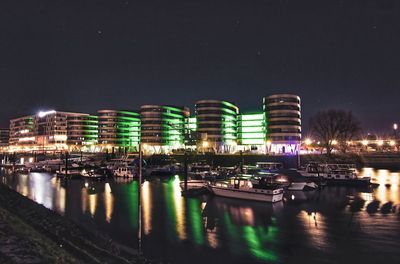 Boats moored in river against illuminated buildings in city at night