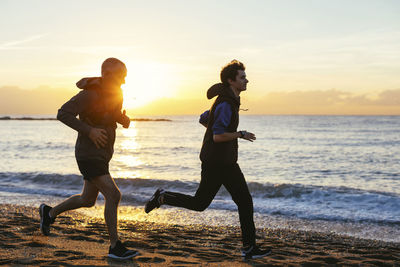 Father and son jogging at beach against sea during sunset