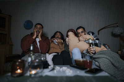 Frightened multiracial friends watching scary movie in cabin