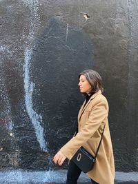 Side view of young woman walking against wall