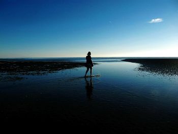 Woman walking on shore against blue sky