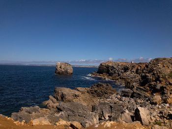 Scenic view of rocks in sea against clear blue sky