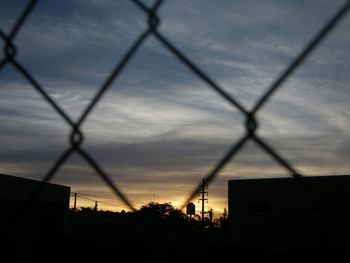 Silhouette chainlink fence against sky during sunset