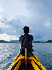 Rear view of man sitting on boat in sea against sky