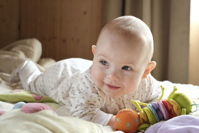 Smiling baby girl learning to crawl and playing with colorful toys in white sunny bedroom.