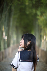 Close-up of young woman looking away while standing against trees