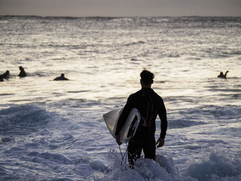 Man with surfboard standing in sea against sky