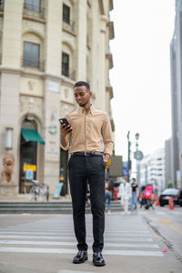 Full length of young man using phone on city street
