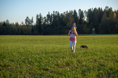 Happy mother carrying son on shoulders while walking on grassy field in park