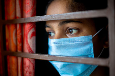 A bored asian young girl wearing a protection surgical face mask at looking through a window