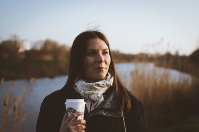 Young woman drinking water against sky