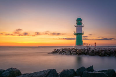 Lighthouse by sea against sky during sunset