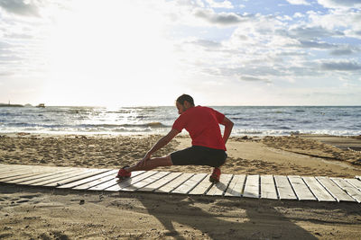 Man stretching leg on boardwalk at beach