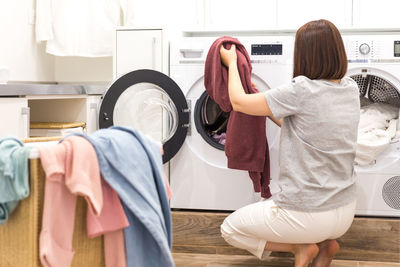 Rear view of removing clothes from washing machine at home