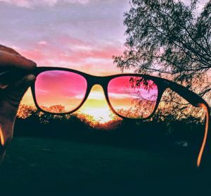 Close-up of sunglasses against trees during sunset