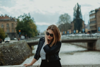 Young woman wearing sunglasses standing against city in background