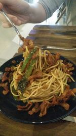 Close-up of hand holding noodles in plate on table