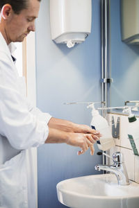 Side view of male doctor washing hands in hospital bathroom