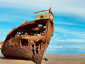 Abandoned boat on beach against sky