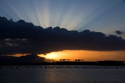 Scenic view of silhouette mountains by sea against sky during sunset