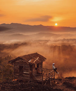 Man by hut against sky during sunrise