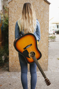 Rear view of woman with guitar standing outdoors