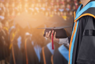 Man holding mortarboard while standing with friends during graduation ceremony