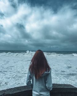 Rear view of woman looking at sea against storm clouds