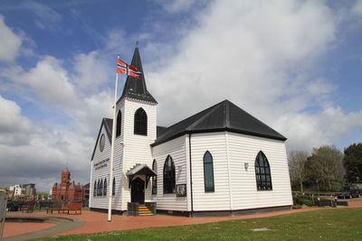 Norwegian church by flag against cloudy sky