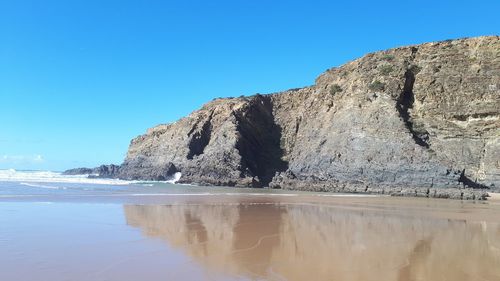 Rock formation in sea against clear blue sky