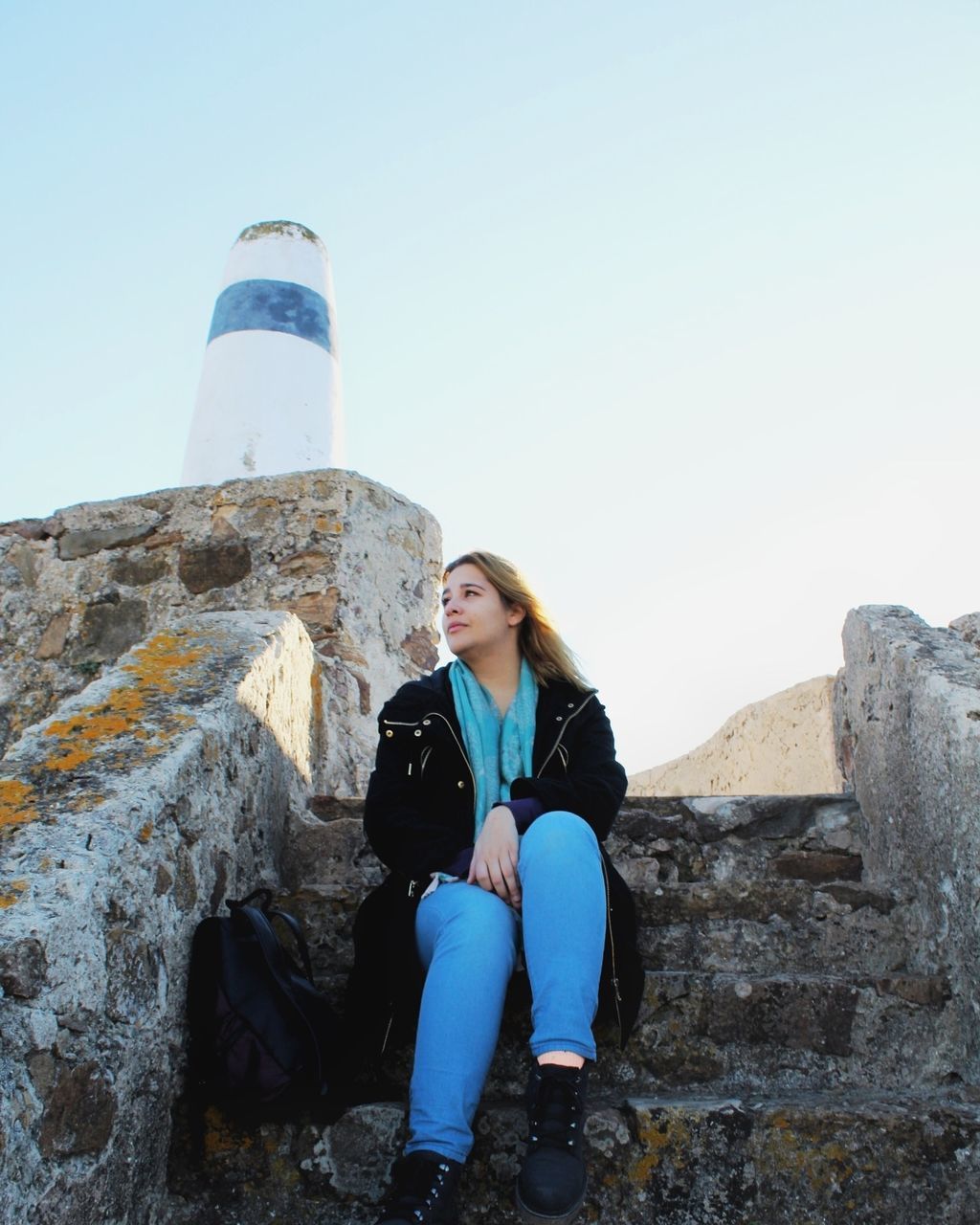 FULL LENGTH OF YOUNG WOMAN SITTING AGAINST BUILT STRUCTURE